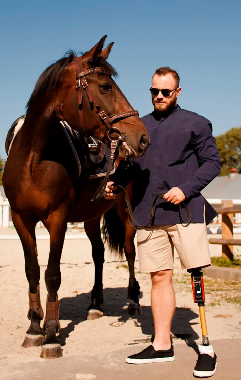 Homem de óculos escuros ao lado de um cavalo, com prótese de perna