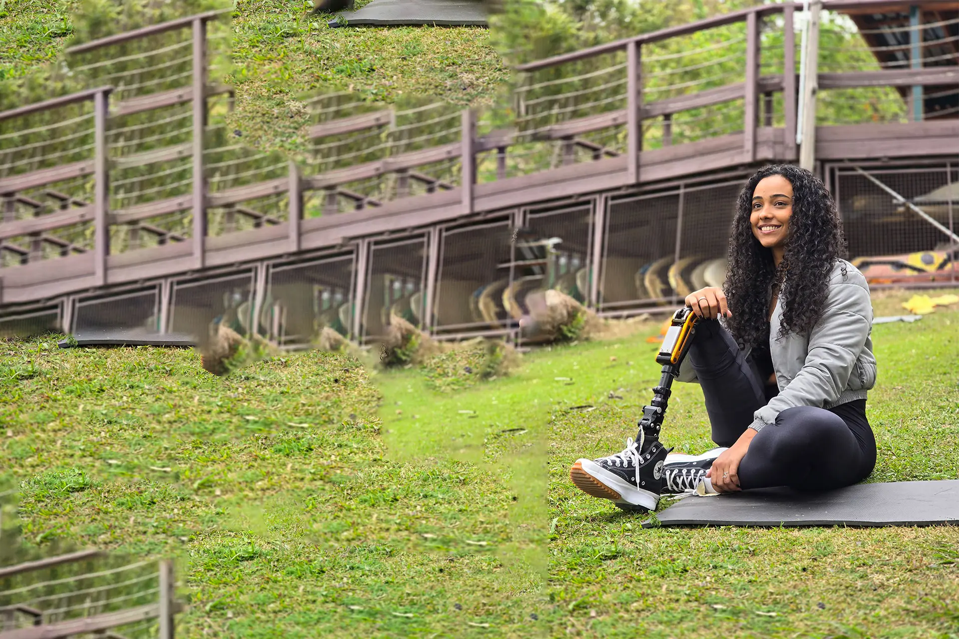 Mulher sorrindo, sentada num gramado, com prótese de perna e tênis