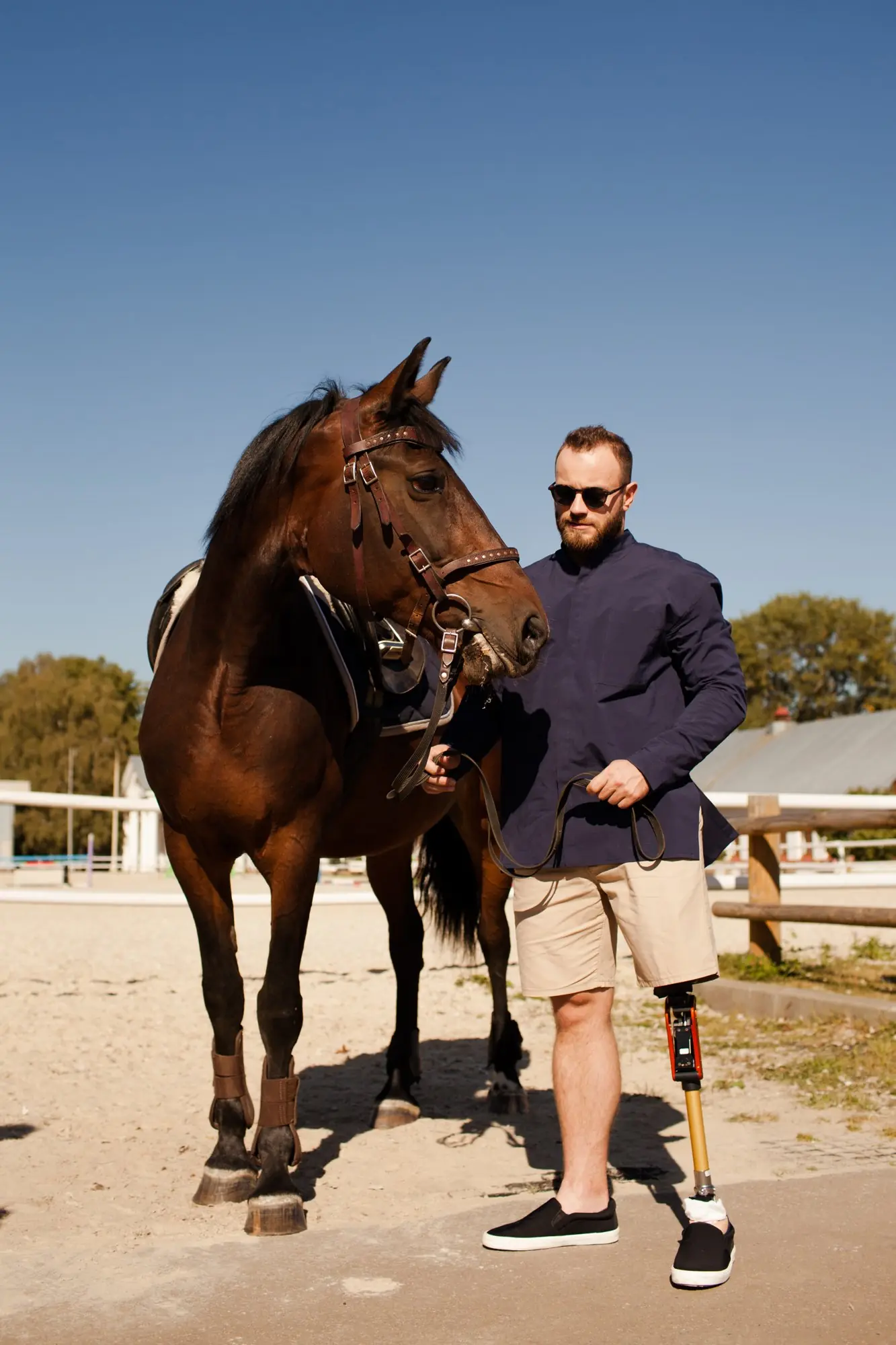 Homem com prótese de perna segurando um cavalo pelas rédeas